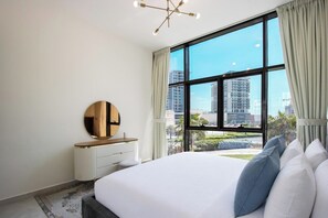 Habitación de hotel moderna con una cama grande, un espejo redondo, un radiador y vistas a la ciudad a través de un ventanal.
