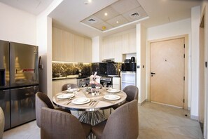 A modern kitchen with a dining area, featuring stainless steel appliances, a marble countertop, and a round dining table with chairs. - Duplex 3BR with Garden Terrace & Glass Lounge (Dubai)