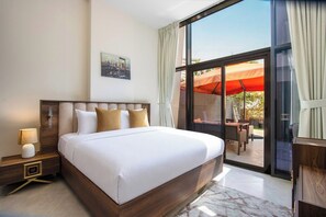 Habitación de hotel con una cama grande, una mesita de noche, una lámpara de pared y un ventanal con vistas a un patio exterior.