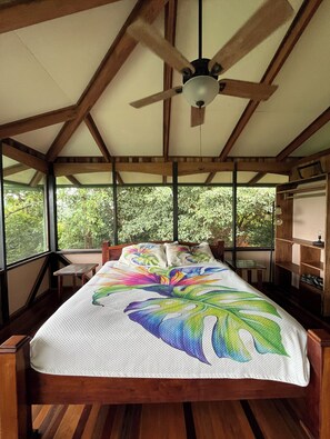 Ein Zimmer mit einem Bett, einem Deckenventilator, einem Fenster und Blick auf Grün.