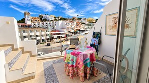 Un balcón con una mesa dispuesta para dos personas, con vistas a una zona residencial y un cielo despejado.
