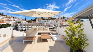 Eine Dachterrasse mit Außenmöbeln, einem großen Sonnenschirm und Blick auf die Stadtlandschaft.