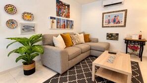 Ein Wohnzimmer mit grauem Sofa, einem Couchtisch, einer Topfpflanze und Wandbildern.