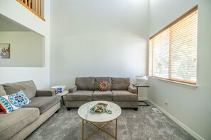 Ein Wohnzimmer mit grauem Sofa, einem runden Couchtisch und einem Fenster mit Jalousien.