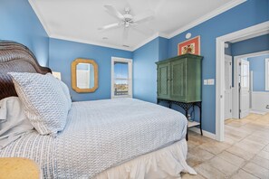 A bedroom with a bed, a ceiling fan, a window with blinds, a green cabinet, and a door leading to another room. - Oceanfront 2BR Condo | Pool + Covered Deck + Easy Beach Access (Pine Knoll Shores)