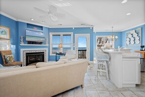 A living room with a fireplace, a television, and a view of the ocean through the windows. - Oceanfront 2BR Condo | Pool + Covered Deck + Easy Beach Access (Pine Knoll Shores)