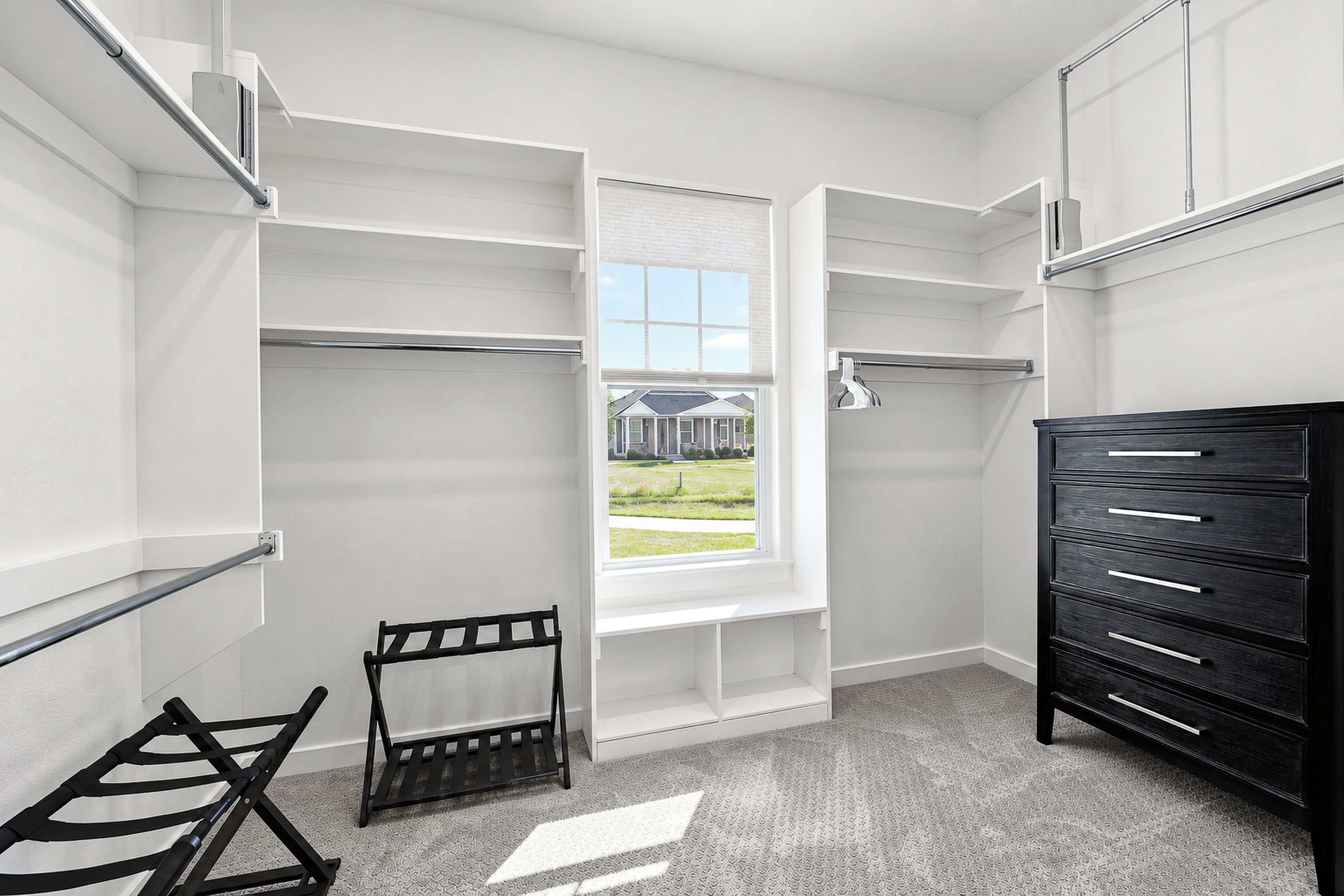A walk-in closet with open shelving, a black dresser, and a window with a view of a house.
