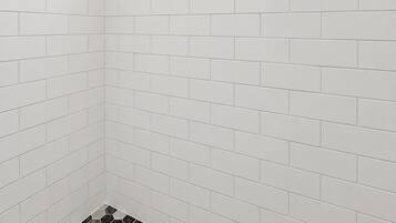 A bathroom with white subway tiles, a black showerhead, a window, and a hexagonal patterned floor.