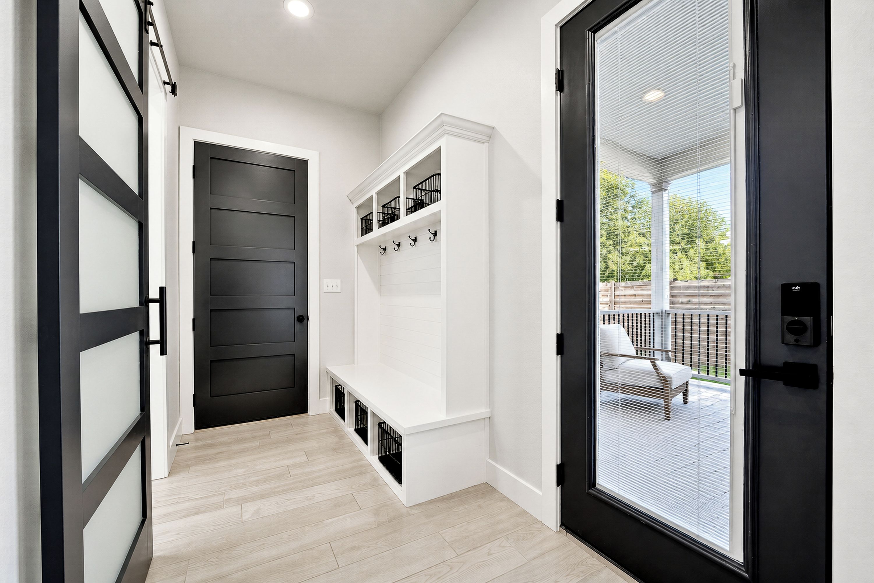 A hallway with a black door, white walls, and a white bench.