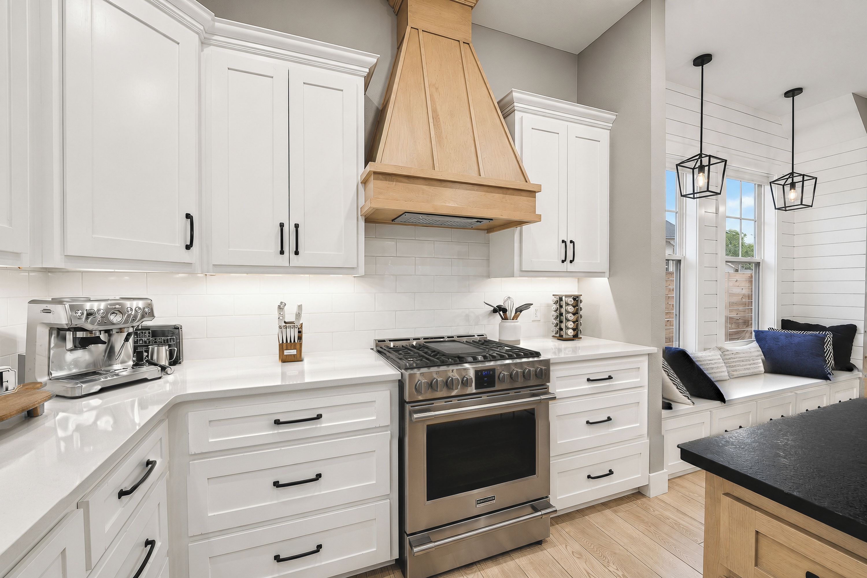A modern kitchen with white cabinetry, a stainless steel stove, and a coffee machine.