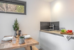 A modern kitchen with a wooden table set for dining, a small Christmas tree, and a window with a view of trees. - Garden Room, Westmeston, Sussex (Westmeston)