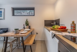 A compact kitchen with a wooden table, a small potted plant, and a cutting board with vegetables. - Garden Room, Westmeston, Sussex (Westmeston)
