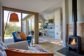 A modern living room with a sofa, a table with a vase of flowers, and a fireplace. - Little Barn, Minsterley, Shropshire (Minsterley)