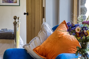 A room with a blue sofa, an orange pillow, a grey throw, a brass lamp, and a vase with flowers. - Little Barn, Minsterley, Shropshire (Minsterley)