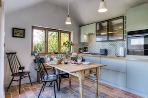 A kitchen with a dining table, chairs, a window with a view of greenery, and a tiled backsplash. - Little Barn, Minsterley, Shropshire (Minsterley)