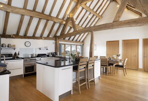 A spacious kitchen with a large island, wooden beams, and a view of the outdoors through a window. - Wall Hills Barn, Bromyard, Herefordshire (Bromyard)
