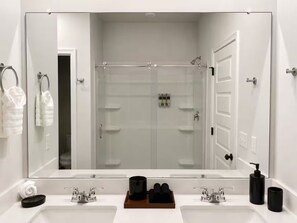 Une salle de bain moderne avec deux vasques, un grand miroir, une douche à parois de verre et un porte-serviettes.