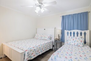 A bedroom with two beds, a ceiling fan, a nightstand, and a window with curtains. - SeaSpray 305 | Oceanview Condo w/ Pool (Atlantic Beach)