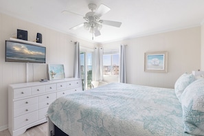 A bedroom with a bed, a dresser, a ceiling fan, a TV, and a window with curtains. - SeaSpray 305 | Oceanview Condo w/ Pool (Atlantic Beach)