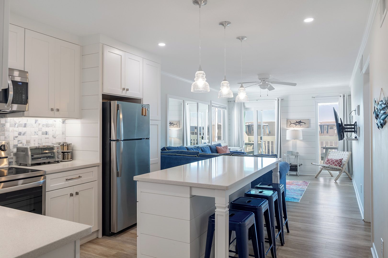 A modern kitchen with stainless steel appliances, a central island with bar stools, and a seating area with a blue sofa.