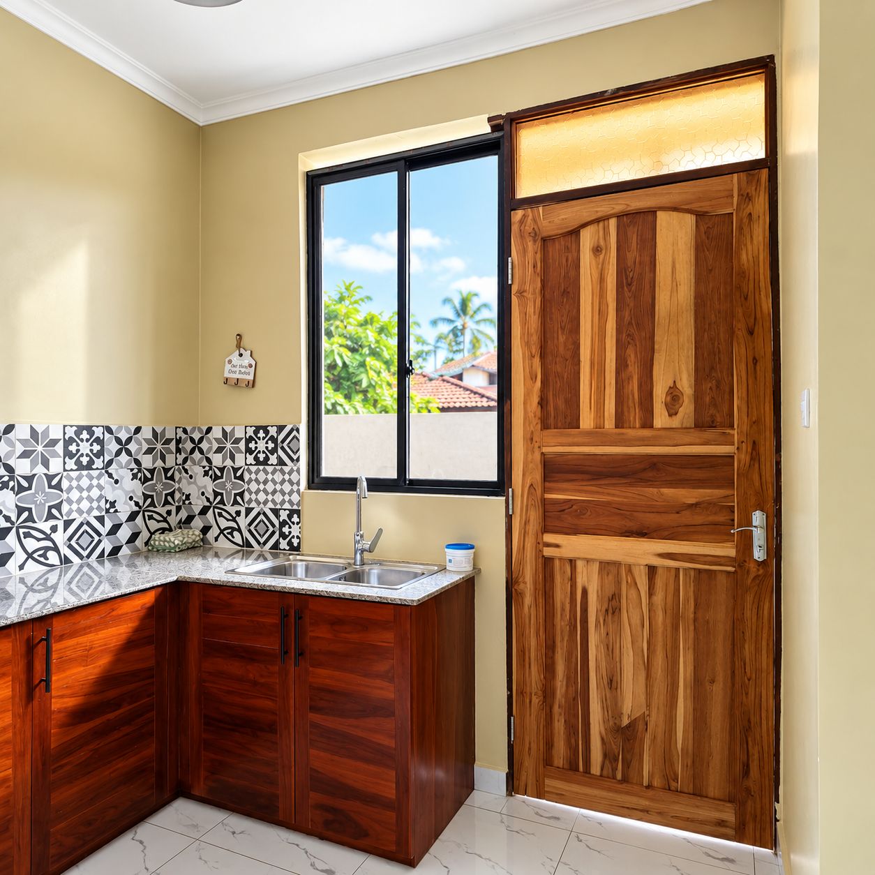 A kitchen with a wooden door, a window with a view, and a tiled backsplash.