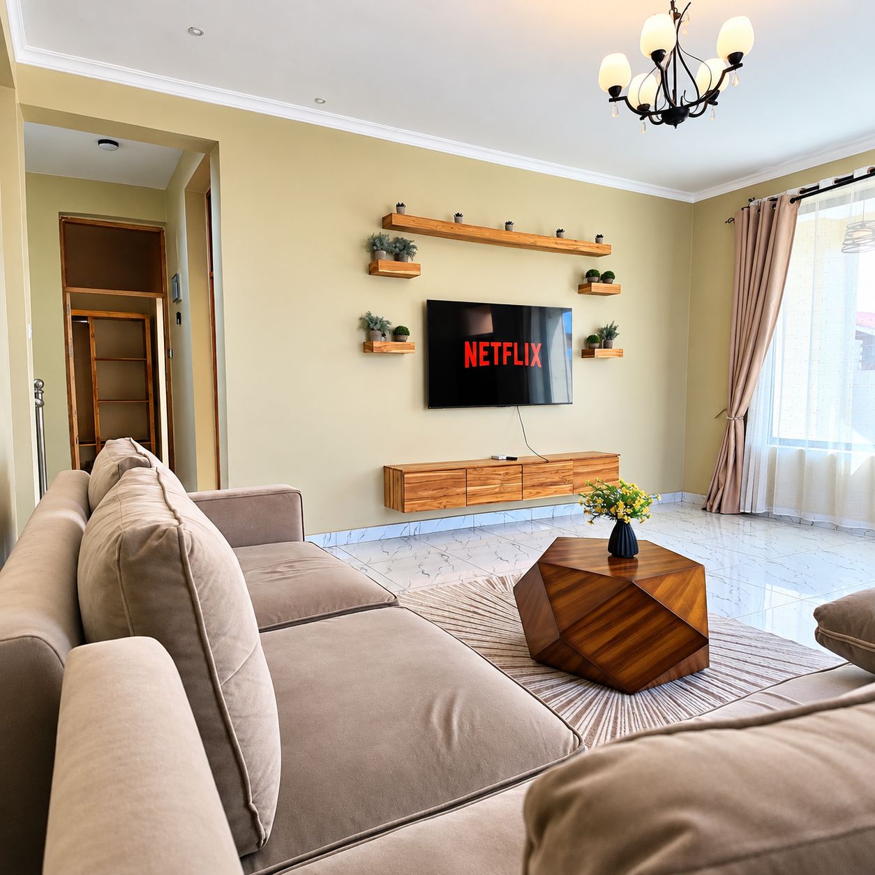 Una sala de estar con un televisor de pantalla plana grande montado en la pared, un mueble bajo de madera y un sofá color beige.