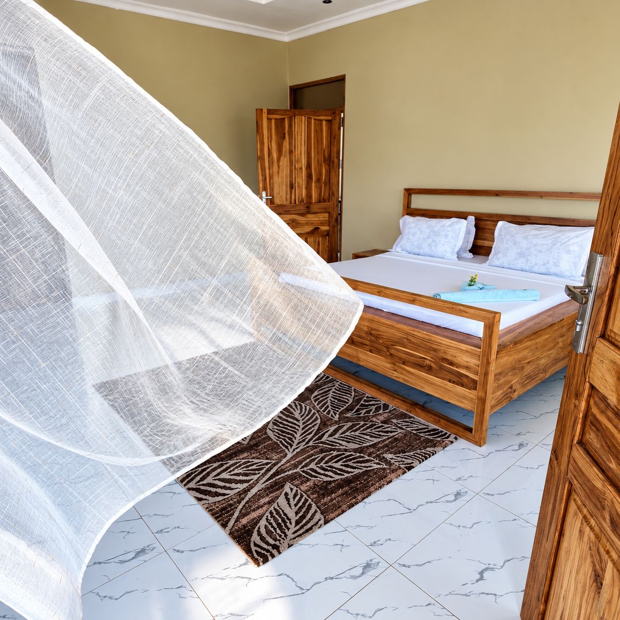 Ein Schlafzimmer mit einem hölzernen Bett, einem weißen Moskitonetz und einem gemusterten Teppich.