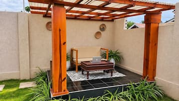Ein überdachter Patio-Bereich mit einer Holz-Pergola, einer Couch, einem Couchtisch mit einem Laptop und topfgestellten Pflanzen.