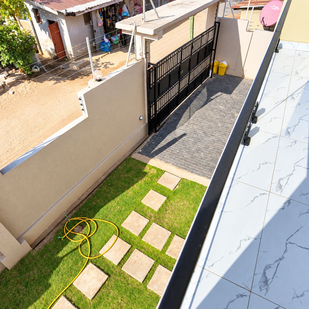 A rooftop terrace with a paved area, a small garden, and a black gate.