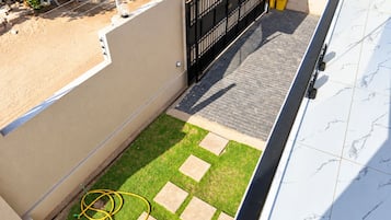 A rooftop terrace with a paved area, a small garden, and a black gate.