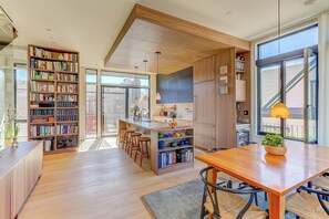 A modern kitchen with wooden cabinets, a central island, bar stools, and a large window providing natural light. - L'Avenir on Oak | Steps from Old Town Square (Fort Collins)