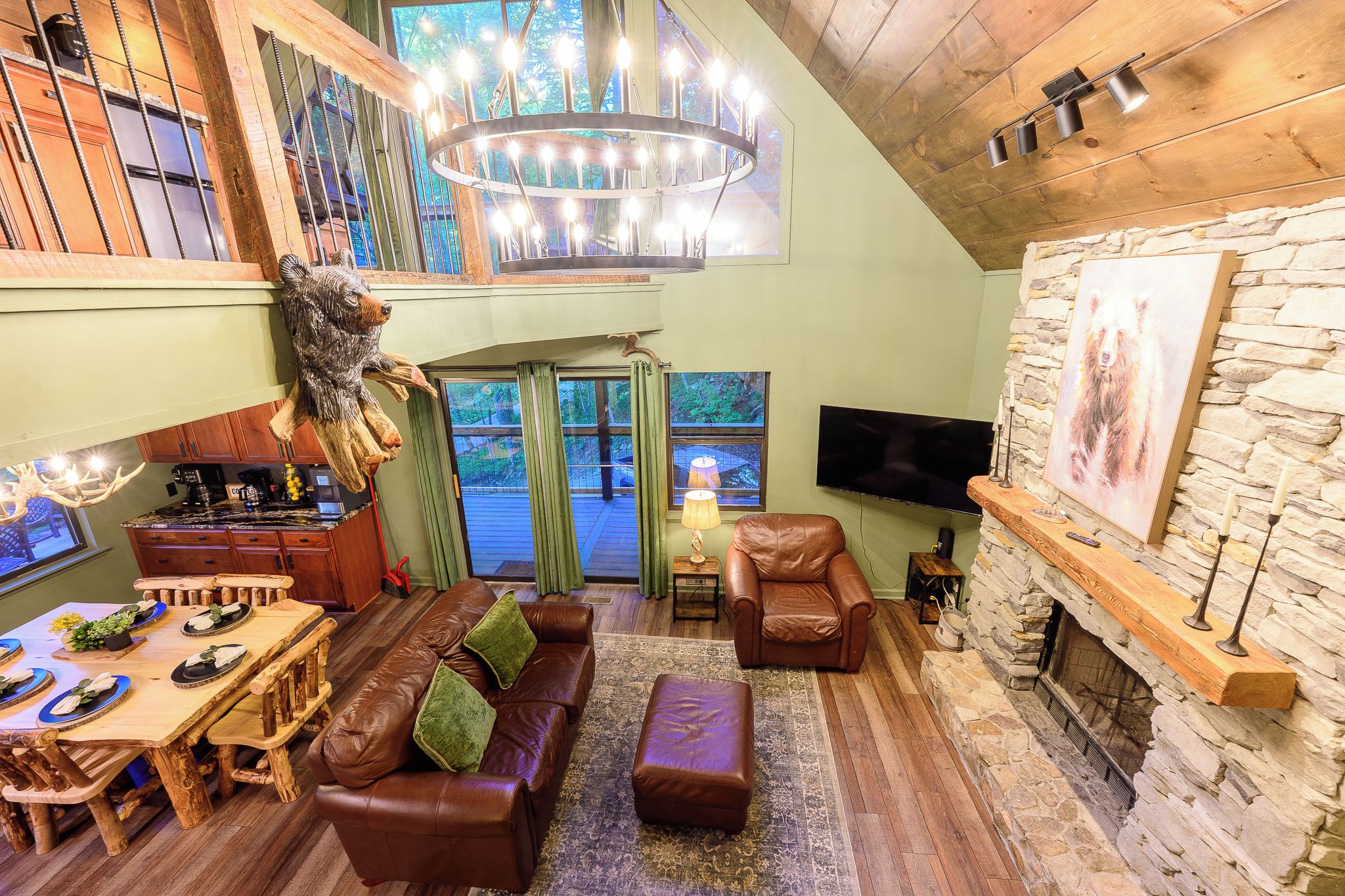 A cozy living room with a fireplace, leather furniture, a dining area, and a large window overlooking greenery.