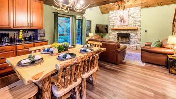 Une table à manger en bois avec des chaises, une cheminée, un mur en pierre et un téléviseur.