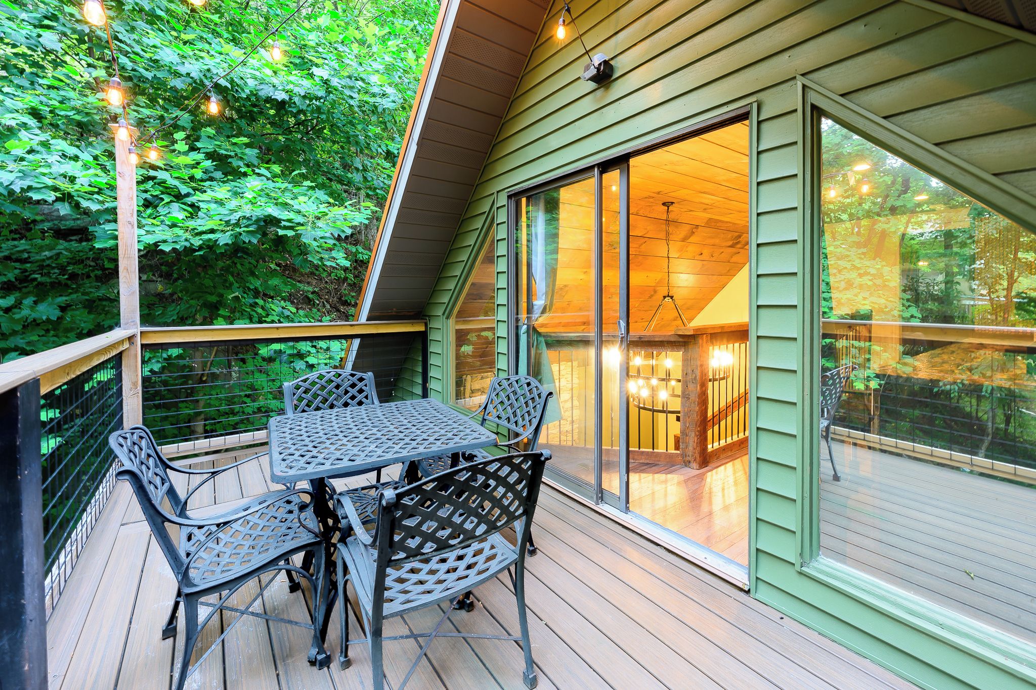 Une terrasse en bois avec une table et des chaises, une porte vitrée donnant sur l’intérieur et une vue sur l’extérieur.