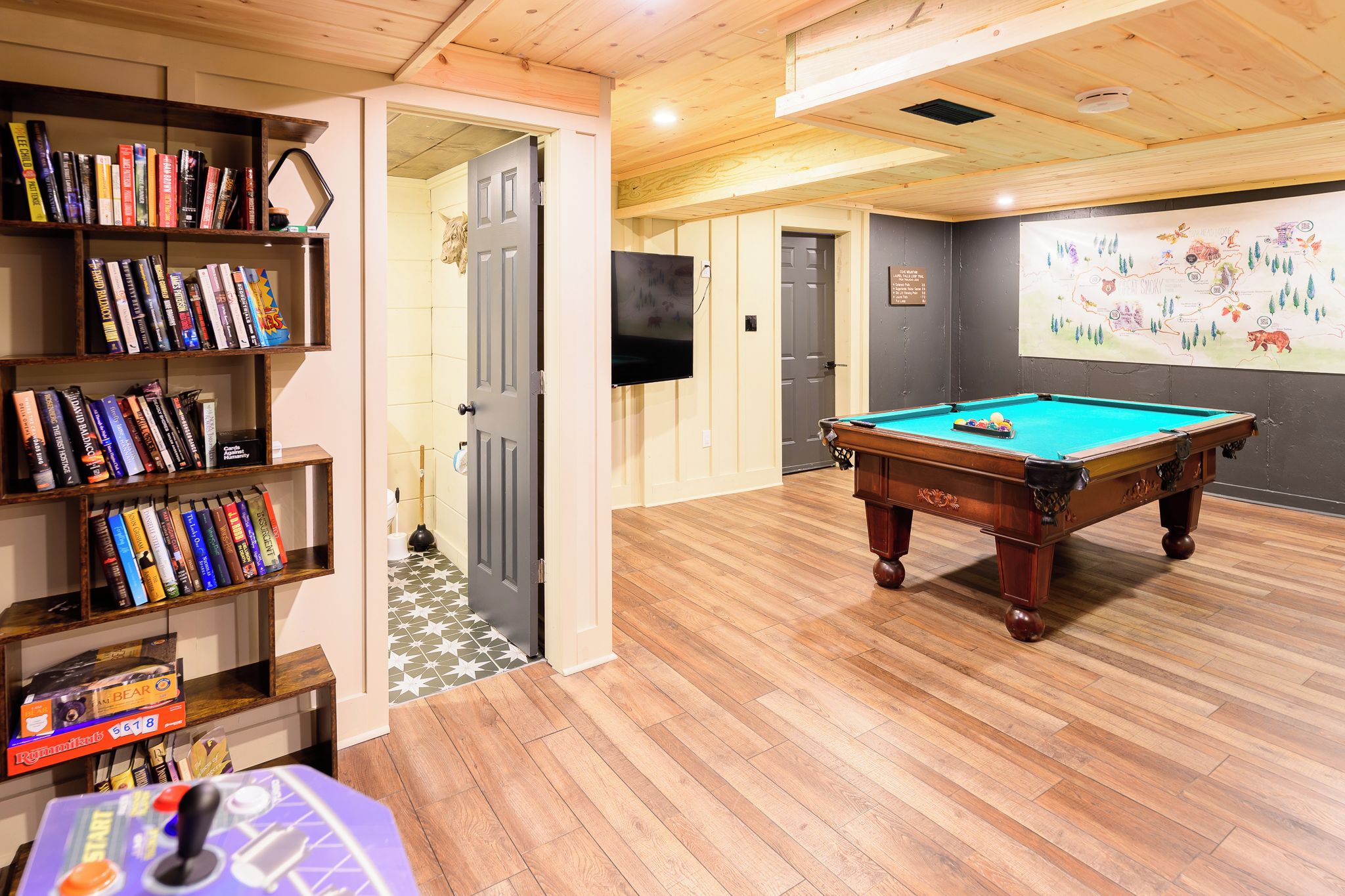 A room with a pool table, a bookshelf with various books, and a wall with a map.