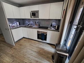 Une cuisine compacte avec des meubles blancs, un four à micro-ondes, un évier et une poubelle en acier inoxydable.