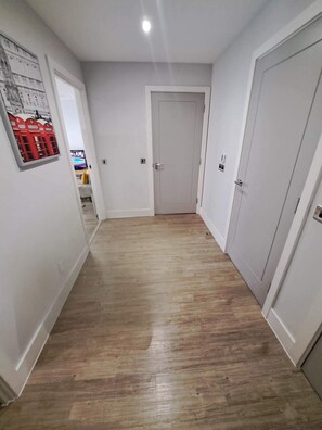 A hallway with wooden flooring, white walls, and a door at the end. - City Court - Stylish 1BR Home in the City (London)