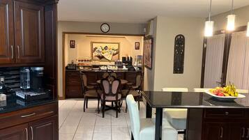 Una cocina con armarios de madera oscura, una cafetera, un comedor con mesa y sillas, y un frutero en la isla.