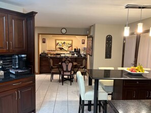 A kitchen with dark wooden cabinets, a coffee machine, a dining area with a table and chairs, and a fruit bowl on the island.