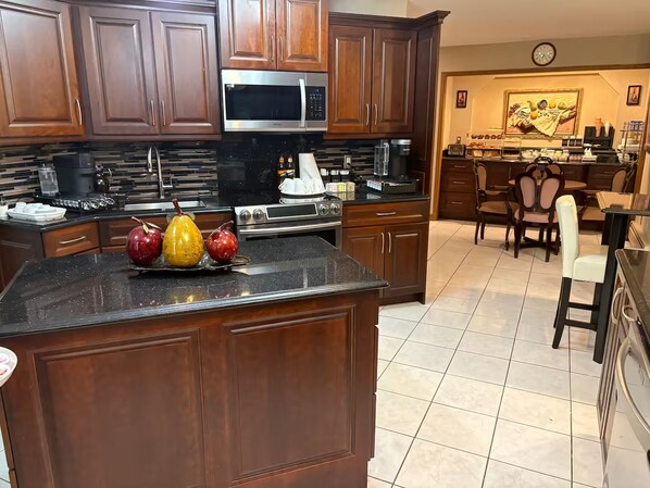 A kitchen with dark wood cabinets, a stainless steel microwave, a coffee maker, and a fruit bowl on the counter.