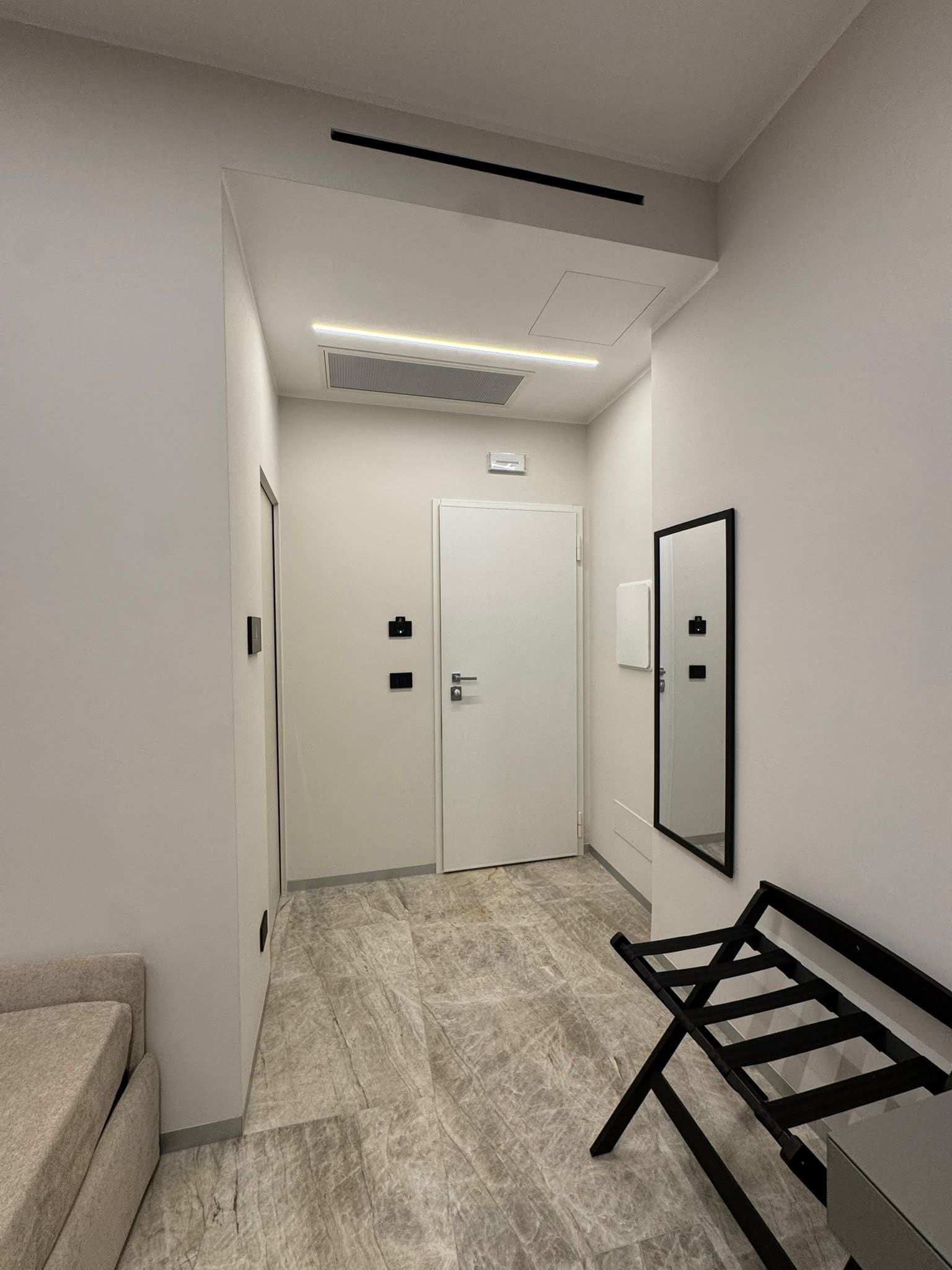 A hallway with a bed, a door, and a mirror.