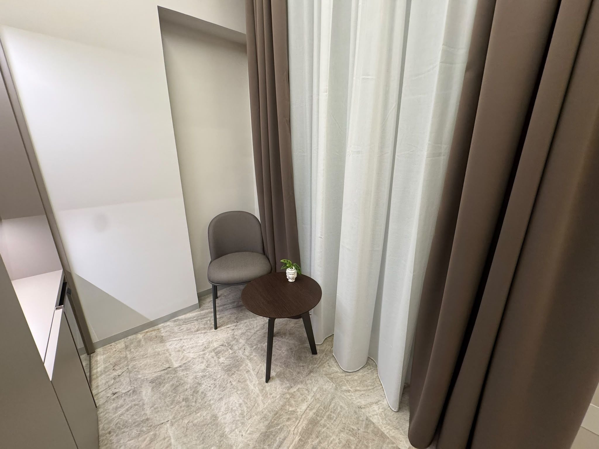 A modern room with a small round table, a grey chair, and a potted plant.
