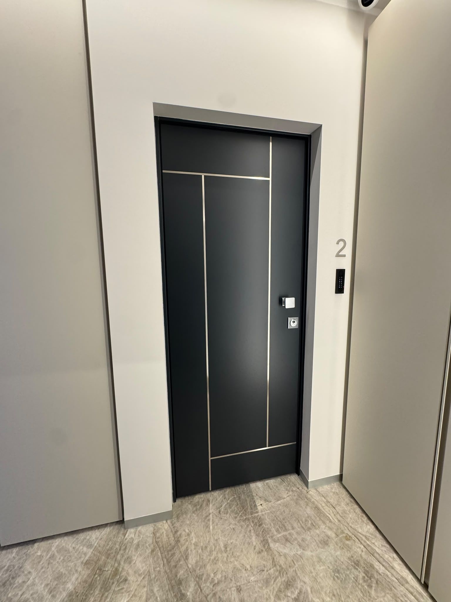 Un ascenseur moderne avec une porte noire, un écran numérique et le chiffre « 2 » peint sur le mur.