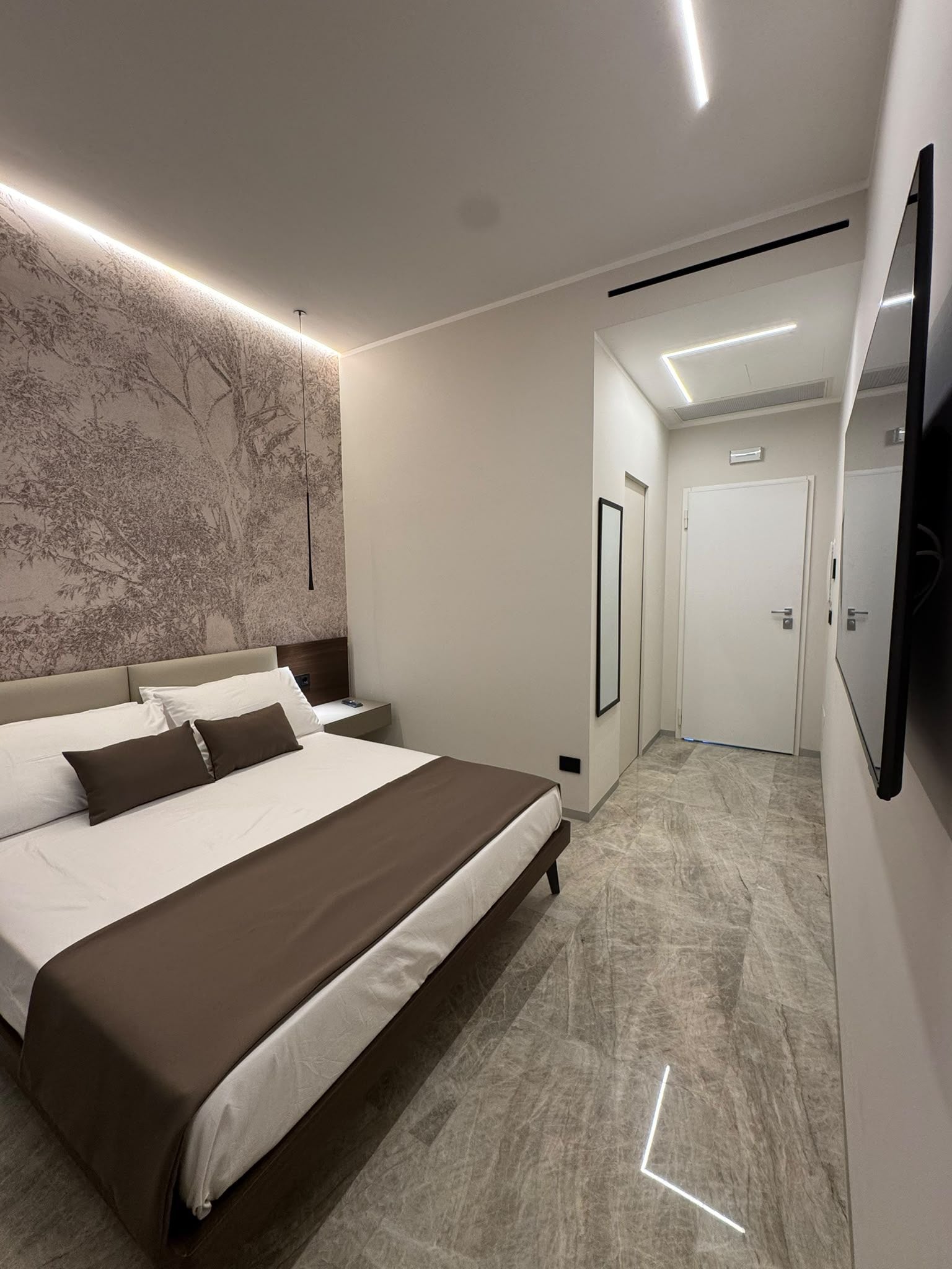 Ein modernes Schlafzimmer mit einem großen Bett, einem an der Wand befestigten Fernseher und einem Flur, der zu einer Tür führt.