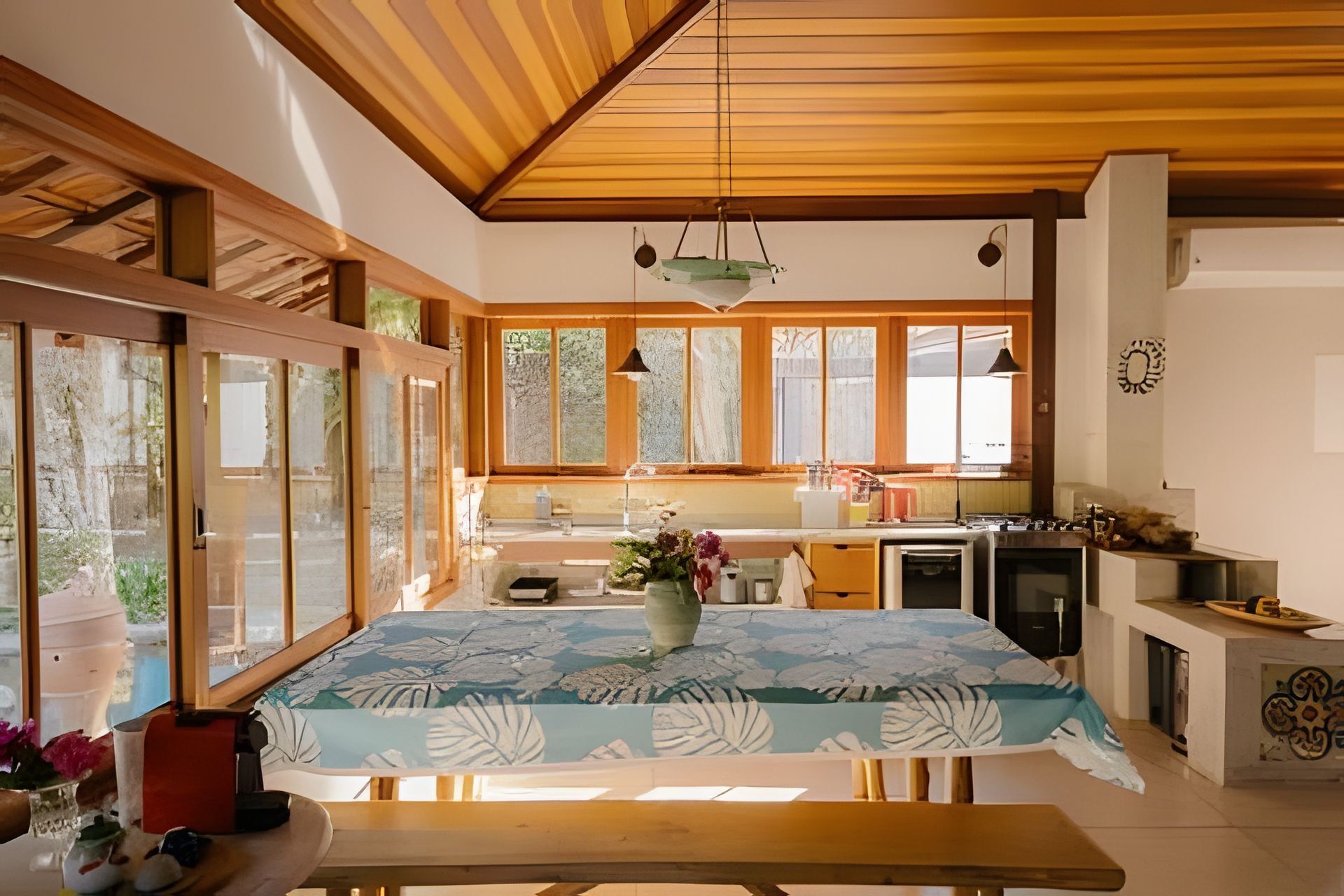 A modern kitchen with wooden beams, large windows, and a dining area with a table.