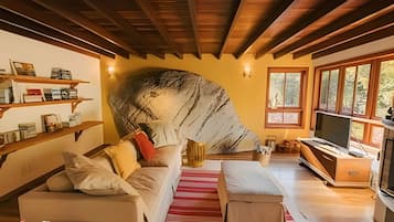 Uma sala de estar acolhedora com um grande elemento rochoso, vigas de madeira, um sofá, uma TV e uma estante.