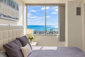 A hotel room with a large window, a bed, a nightstand, and a painting on the wall. - Ocean & Marina View Condo, Free Parking, Waikiki (Honolulu)