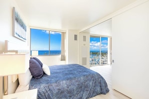 Ein Schlafzimmer mit Bett, Nachttisch, Fenster mit Meerblick und einer Tür zu einem Balkon.