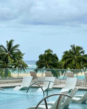 Un espace piscine avec des chaises longues et une vue sur la plage et l’océan.