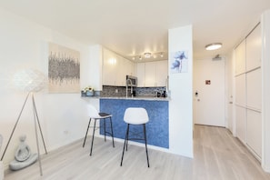 Eine moderne Küche mit blauer Arbeitsplatte, zwei weißen Barhocker und einem Essbereich.